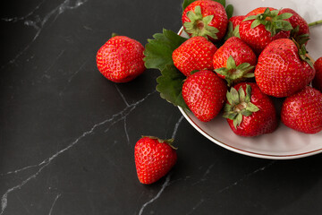 Fresh strawberries in plate on marble black table. Fresh nice strawberries. Strawberry field on fruit farm. Heap of Red strewberry on plate close up. Juice strawberry. Strawberry field on fruit farm.