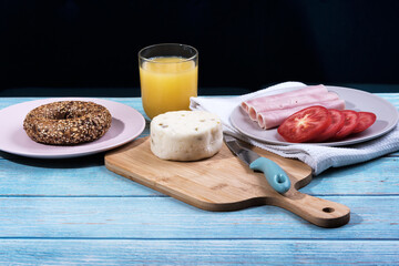 Breakfast served at blue wooden table with juice, ham, pecorino cheese, tomato and corn bread pretzel. Continental delicious healthy breakfast table