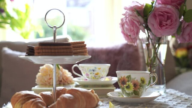Traditional English tea time, Afternoon tea ceremony with cuppa tea, croissants, crackers and biscuits on hight tea stand in pink pastel. Cozy sence of afternoon party in conservatory room