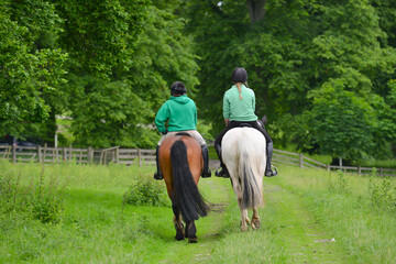 Rear view of two  young women riding together in the English countryside, enjoying being outdoors in nature .