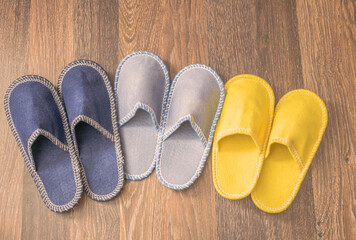 Three pairs of colorful slippers are on the floor. Different sneakers for all family members are on a woody background. Shoes for dad, mom and baby. The concept of a cosiness.