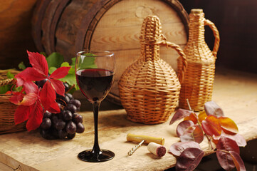 Glass of red wine, bottle, bunch of grapes on the background of a wine barrel