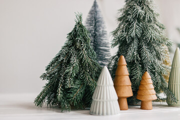Christmas little trees on white background. Winter forest, festive modern decor. Happy holidays. Miniature ceramic,wooden, snowy and handmade pine trees. Season greetings. Merry Christmas. © sonyachny