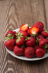Fresh strawberries in a plate on wooden table. Fresh nice strawberries. Strawberry field on fruit farm. Heap of Red strewberry on plate close up. Juice strawberry. Strawberry field on fruit farm.