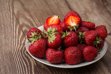 Fresh strawberries in a plate on wooden table. Fresh nice strawberries. Strawberry field on fruit farm. Heap of Red strewberry on plate close up. Juice strawberry. Strawberry field on fruit farm.