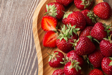 Fresh strawberries in a wooden plate on wooden table. Fresh nice strawberries. Strawberry field on fruit farm. Heap of Red strewberry on plate. Juice strawberry. Strawberry field on fruit farm.