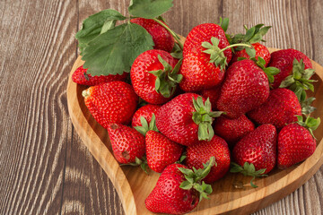 Fresh strawberries in a wooden plate on wooden table. Fresh nice strawberries. Strawberry field on fruit farm. Heap of Red strewberry on plate. Juice strawberry. Strawberry field on fruit farm.