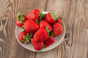 Fresh strawberries in a plate on wooden table. Fresh nice strawberries. Strawberry field on fruit farm. Heap of Red strewberry on plate close up. Juice strawberry. Strawberry field on fruit farm.