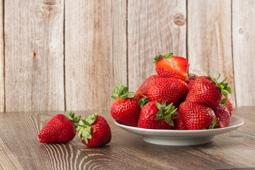 Fresh strawberries in a plate on wooden table. Fresh nice strawberries. Strawberry field on fruit farm. Heap of Red strewberry on plate close up. Juice strawberry. Strawberry field on fruit farm.