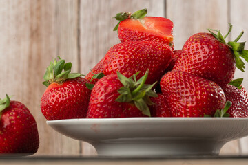 Fresh strawberries in a plate on wooden table. Fresh nice strawberries. Strawberry field on fruit farm. Heap of Red strewberry on plate close up. Juice strawberry. Strawberry field on fruit farm.