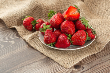 Fresh strawberries in a plate on wooden table. Fresh nice strawberries. Strawberry field on fruit farm. Heap of Red strewberry on plate close up. Juice strawberry. Strawberry field on fruit farm.