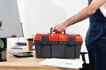 cropped view of repairman with toolbox on office desk with papers and coffee to go