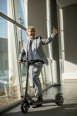 Mature businessman standing by the office window with electric scooter