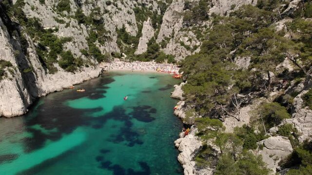 Breathtaking view of Calanque d&rsquo;En-Vau, a beautiful blue lagoon with a white sand beach and many tourists, surrounded by cliffs, pines, must-see destination near Marseille in France 