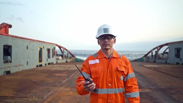 Filipino deck Officer on deck of vessel or ship , wearing PPE personal protective equipment. He speaks to VHF walkie-talkie radio in hands. Dream work at sea