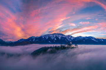 Mystischer Sonnenuntergang über dem Nebel mit Kirchlein auf einem Berg