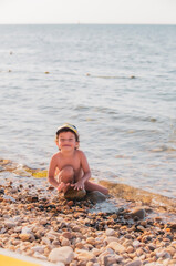 Little boy on a pebble beach. a little boy sits on the beach and looks at camera