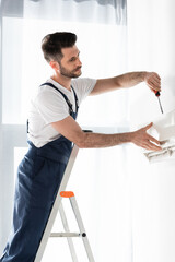 handsome repairman standing on stepladder and fixing air conditioner with screwdriver