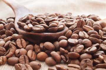 coffee beans in a wooden spoon and around it on a sackcloth background