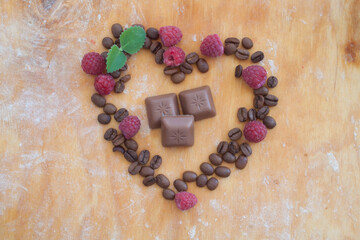 heart shaped coffee beans and raspberry with chocolate in the middle on wooden background