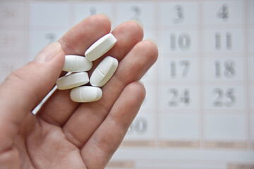 selective focus at the hand and pills with the blurred calendar at the background