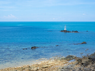 Fototapeta na wymiar Lighthouse in bright sunny summer day in the sea of Thailand. Rocky coast under the blue sky with cloud and calm water.