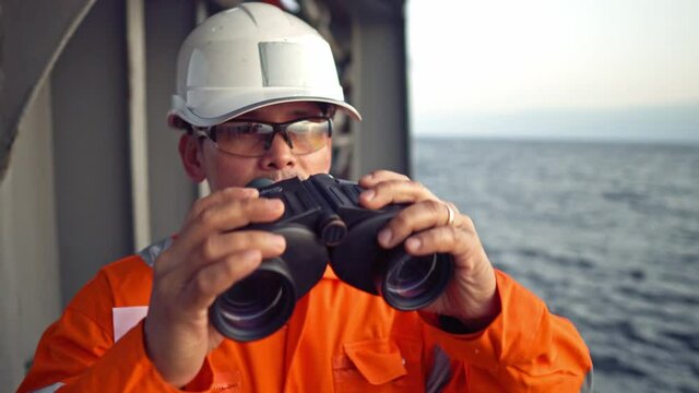 Filipino deck Officer on deck of vessel or ship , wearing PPE personal protective equipment. He is looking through binoculars.
