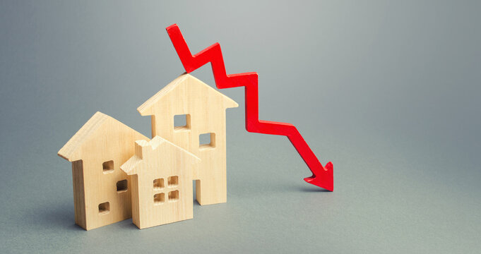 Miniature wooden houses and a red arrow down. The concept of low cost real estate. Lower mortgage interest rates. Falling prices for rental housing and apartments. Reducing demand for home buying