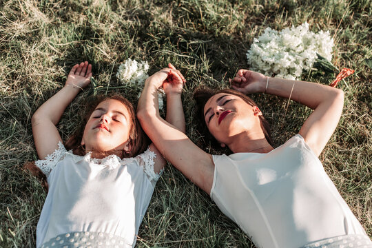 Mom and her daughter lying on the grass with arms above theirs heads