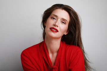 Happy and beautiful young caucasian woman wearing red top and red lipstick. Posing over white background.