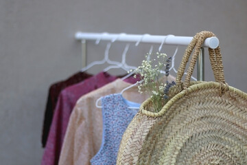 Clothing rack with colorful floral dresses and wicker bag with flowers. Selective focus.