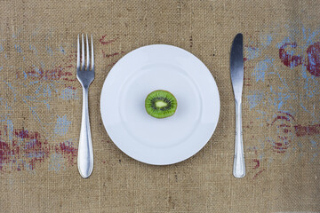Half a kiwi on a white plate with a fork and a knife.