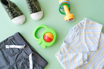 Kit of clothes, footwear and toys for infant baby boy. Flat lay design. Baby goods on green background.