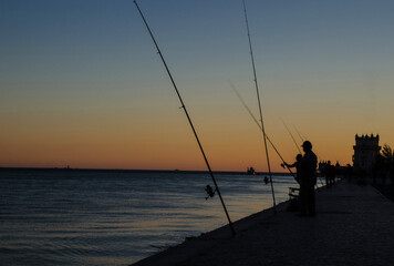 Fishermen silhouette at sunset near Belem tower, in Lisbon, Portugal