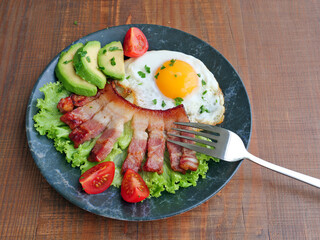 Bacon with fried egg, avocado and vegetables on plate. Low-carb ketogenic breakfast