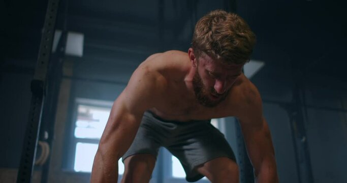 Wide shot of young Caucasian extreme weightlifting athlete man working out with heavy barbell in large hardcore gym hall.