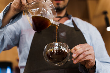 Close up pouring coffee in double glass cup in cafe by handsome bearded barista. Coffee brewing syphon and aeropress alternative methods. Advert for social networks for cafe and restaurant.