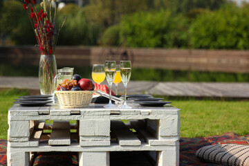 Catering in nature. Picnic. Table setting in nature near the lake. Summer, sunny day. Fruit, drinks, flowers on a white wooden table. Background image, copy space