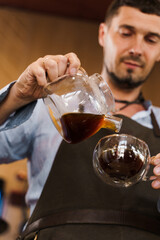 Close-up pouring coffee in double glass cup in cafe by handsome bearded barista. Coffee brewing syphon and aeropress alternative methods. Advert for social networks for cafe and restaurant.