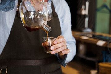 Close-up pouring coffee in double glass cup in cafe by handsome bearded barista. Coffee brewing syphon and aeropress alternative methods. Advert for social networks for cafe and restaurant.