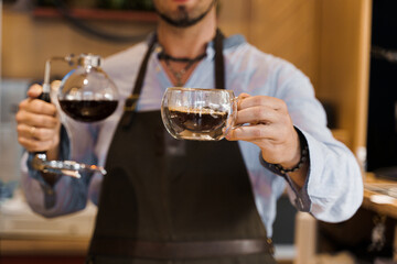 Syphon alternative method of making coffee. Barista gives hot coffee in double glass cup to customers. Coffee brewing in cafe. Scandinavian method of coffee making.