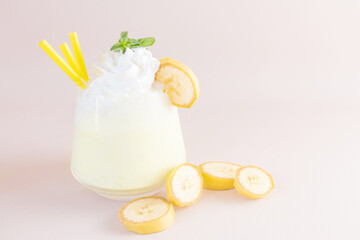 Banana milkshake on a light background in transparent glass. Nearby are slices of banana. The concept of delicious fresh drinks, healthy food for breakfast and snacks.