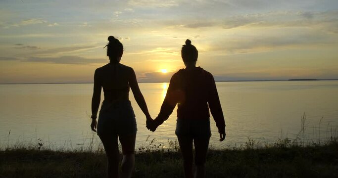 Girls Hold Hands Strongly. Go to Seashore. Amazing View. Setting Sun. Silhouettes of Lovers. Sun Rays. Evening. Summer. Love on Vacation. Found each other. Romance. Magic Moment. Happiness. LGBT