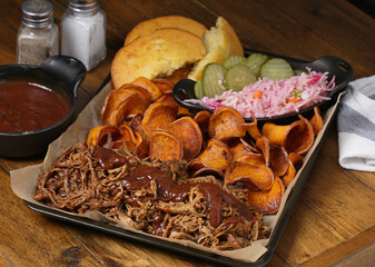 Platter of BBQ pulled pork with fresh sweet potato chips, cornbread, vinegar slaw , and pickle chips
