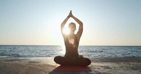 The girl sits in a lotus position, raises her hands up, joining them in her palms, and lowers down, holding in front of her. Human body and nature harmony.