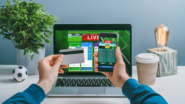 Front view of a man making bets online at bookmaker's website and mobile application using laptop and smartphone
