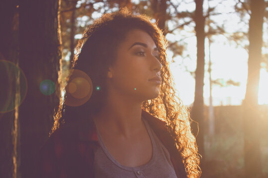 Menina adolescente negra com cabelos cacheados volumosos, ao p&ocirc;r do sol, em uma floresta. Beleza afro, beleza negra.
Clima de outono