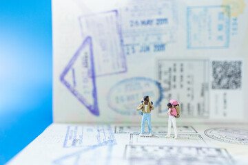 Travel concepts. Two black traveler miniature figures people with backpack standing on passport with many country immigration stamps with blue background.