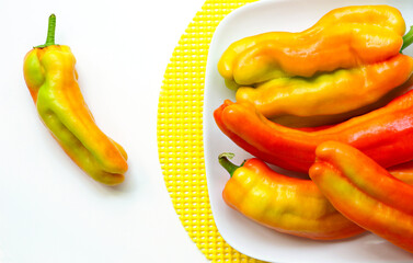 Multicolored red, orange, yellow, and green long peppers on minimalist white surface