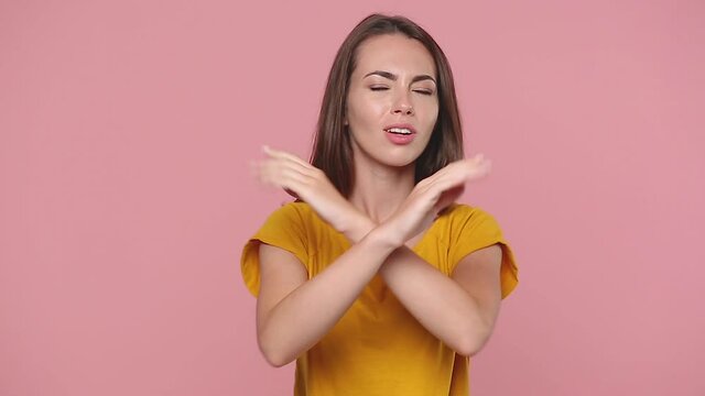 Nervous young woman girl 20s years old in yellow t-shirt posing isolated on pink background studio. People lifestyle concept. Look camera covering ears with hands say blah blah bla do not wanna listen